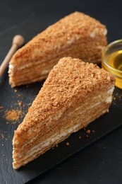 Slices of delicious layered honey cake served on black table, closeup