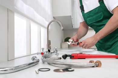 Professional plumber fixing water tap in kitchen, closeup