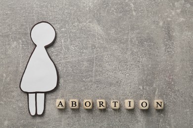 Word Abortion made of wooden cubes and pregnant woman paper cutout on grey background, flat lay. Space for text