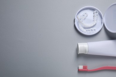 Photo of Bite correction. Toothpaste, brush and dental mouth guards on grey background, flat lay. Space for text