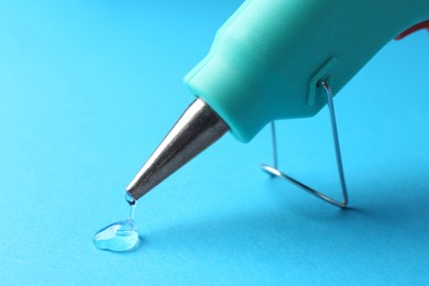 Photo of Melted glue dripping out of hot gun nozzle on light blue background, closeup