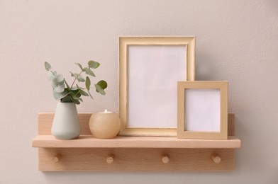 Wooden shelf with photo frames, candle and eucalyptus on beige wall. Interior element