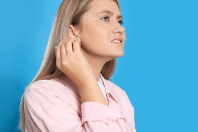 Photo of Young woman cleaning ear with cotton swab on light blue background. Space for text