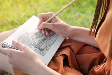 Young woman drawing with pencil in notepad outdoors on sunny day, closeup