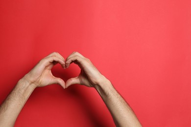 Man making heart with his hands on red background, closeup. Space for text