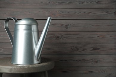 Photo of Metal watering can on table against grey wooden background, space for text