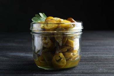 Photo of Glass jar with slices of pickled green jalapeno peppers on black wooden table