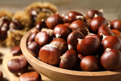 Fresh sweet edible chestnuts in wooden bowl on table, closeup