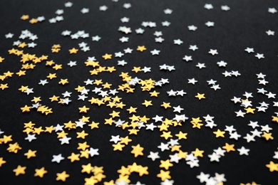 Gold and silver confetti stars on black background, closeup. Christmas celebration