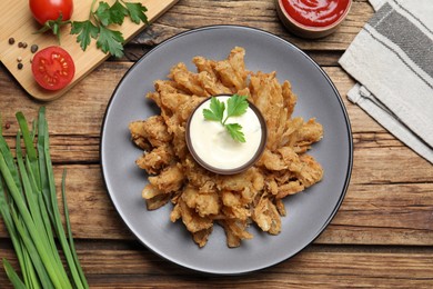 Fried blooming onion with dipping sauce served on wooden table, flat lay