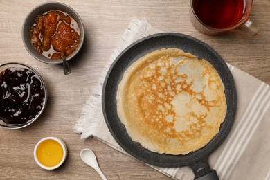 Frying pan with delicious crepe, jams, honey and aromatic tea on wooden table, flat lay