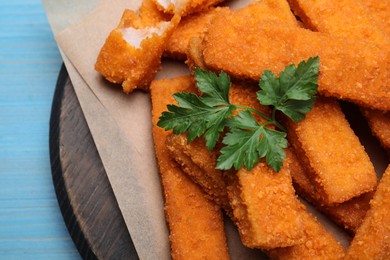 Fresh breaded fish fingers with parsley served on light blue wooden table, top view