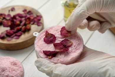 Woman putting flower petals in bath bomb mold at white table, closeup