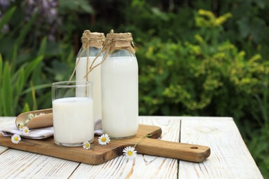 Tasty fresh milk and chamomile flowers on white wooden table outdoors, space for text