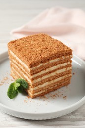 Slice of delicious layered honey cake with mint served on white wooden table, closeup
