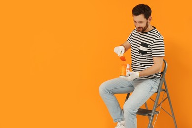 Photo of Designer with painting equipment sitting on folding ladder near freshly painted orange wall, space for text