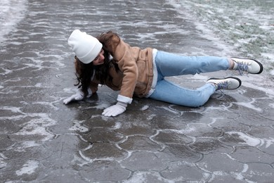 Young woman fallen on slippery icy pavement outdoors