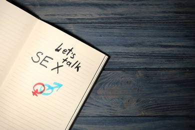 Notebook with phrase "LET'S TALK SEX" and gender symbols on dark wooden background, top view. Space for text