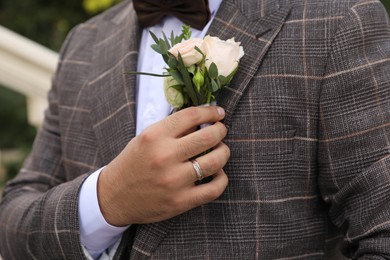 Groom wearing engagement ring with beautiful boutonniere outdoors, closeup. Preparing for wedding
