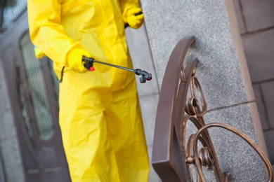 Person in hazmat suit disinfecting railing with sprayer outdoors, closeup. Surface treatment during coronavirus pandemic