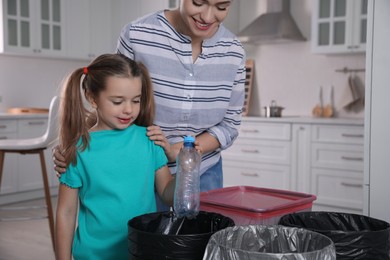 Young woman and her daughter throwing plastic bottle into trash bin in kitchen. Separate waste collection
