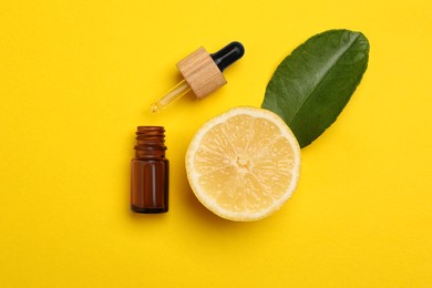 Bottle of citrus essential oil, pipette and fresh lemon on yellow background, flat lay