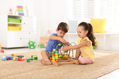 Cute little children playing with bead maze on floor at home. Educational toy