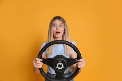 Emotional young woman with steering wheel on yellow background