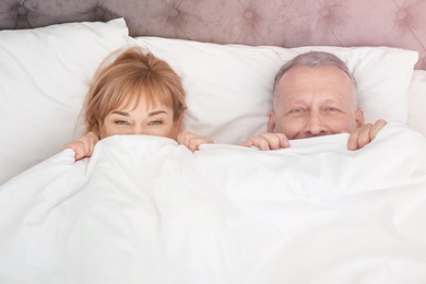 Image of Mature couple hiding together under blanket in bed at home