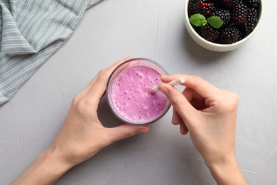 Woman with glass of delicious blackberry smoothie at white table, top view