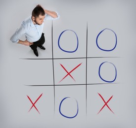 Man and illustration of tic-tac-toe game on grey background, above view. Business strategy concept 