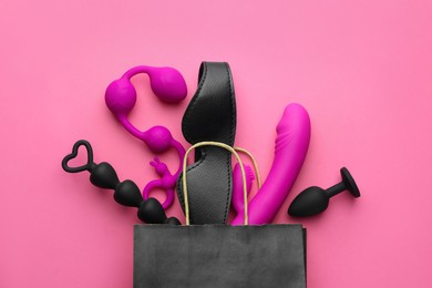 Shopping bag with different sex toys on pink background, flat lay