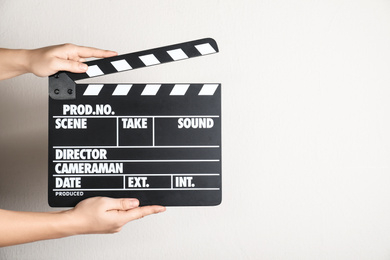 Woman holding clapperboard against light wall, closeup with space for text. Cinema production