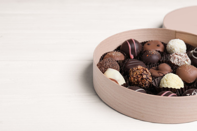 Box with tasty chocolate candies on white wooden table. Space for text