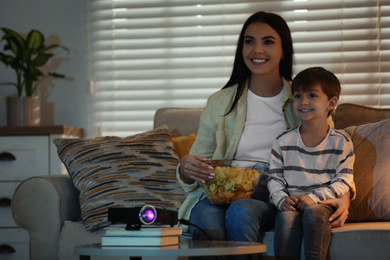 Young woman and her son watching movie using video projector at home. Space for text