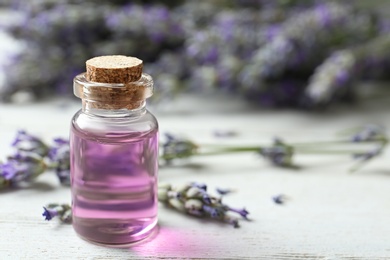Photo of Bottle with essential oil and lavender flowers on white wooden table. Space for text