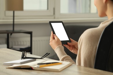 Young woman using e-book reader at wooden table indoors, closeup. Space for text