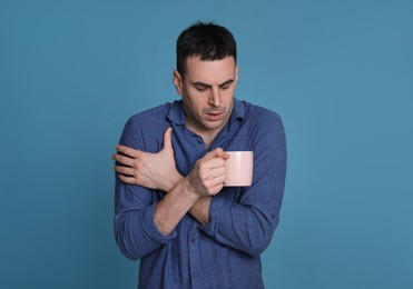 Young man with cup of hot drink suffering from fever on blue background. Cold symptoms