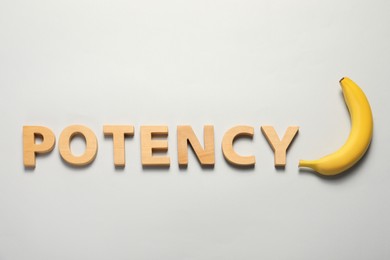 Word Potency made of wooden letters and banana on light grey background, flat lay