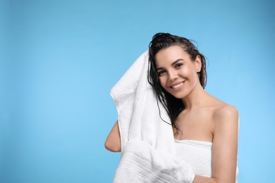 Happy young woman drying hair with towel after washing on light blue background. Space for text