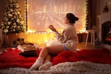 Photo of MYKOLAIV, UKRAINE - DECEMBER 24, 2020: Woman watching Harry Potter and Philosopher's Stone movie via video projector in room. Cozy winter holidays atmosphere