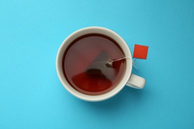 Photo of Tea bag in cup of hot water on light blue background, top view