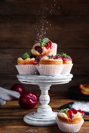 Photo of Delicious sweet cupcakes with plums on wooden table