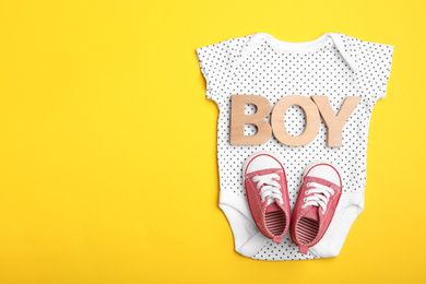 Child's bodysuit, word Boy made with wooden letters and booties on yellow background, top view. Space for text