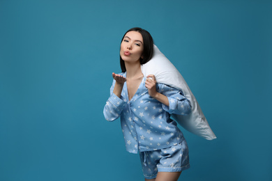 Beautiful Asian woman with pillow blowing kiss on blue background. Bedtime