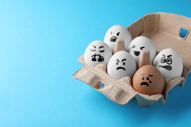 Brown egg with upset face among aggressively disposed white ones in carton box on turquoise background, space for text. Bullying concept
