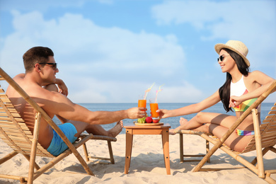 Couple with drinks resting on sunny beach at resort