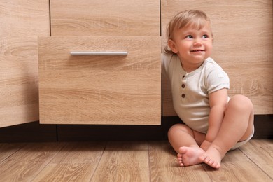 Photo of Little child exploring drawer indoors. Danger situation