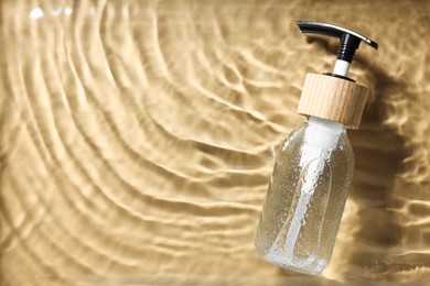 Bottle of cosmetic product in water on beige background, top view. Space for text