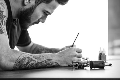 Image of Professional tattoo artist drawing sketch at table indoors. Black and white photography